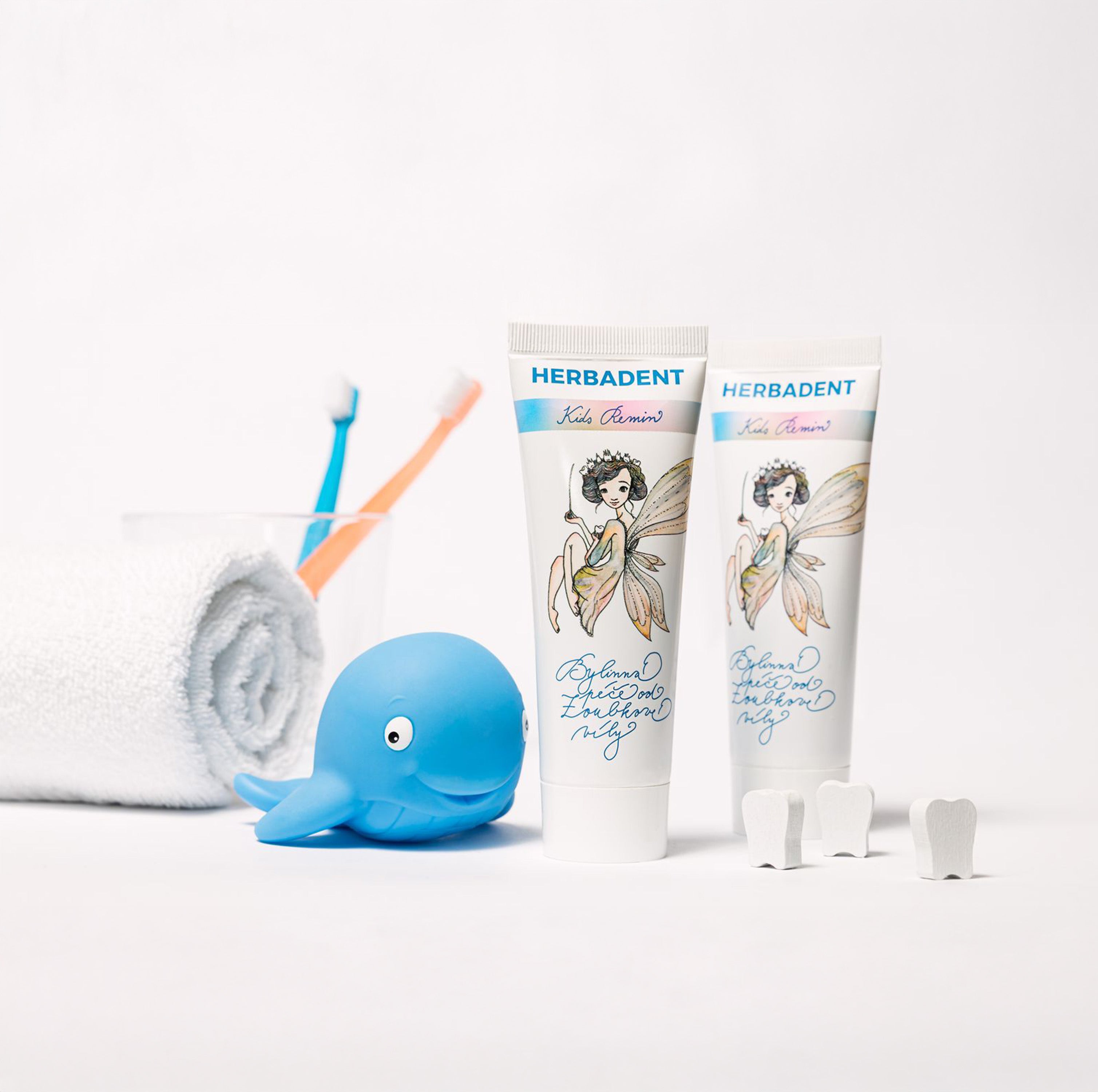 Herbadent children's toothpaste with toothbrushes, a whale-shaped toy, and dental floss on a white background.