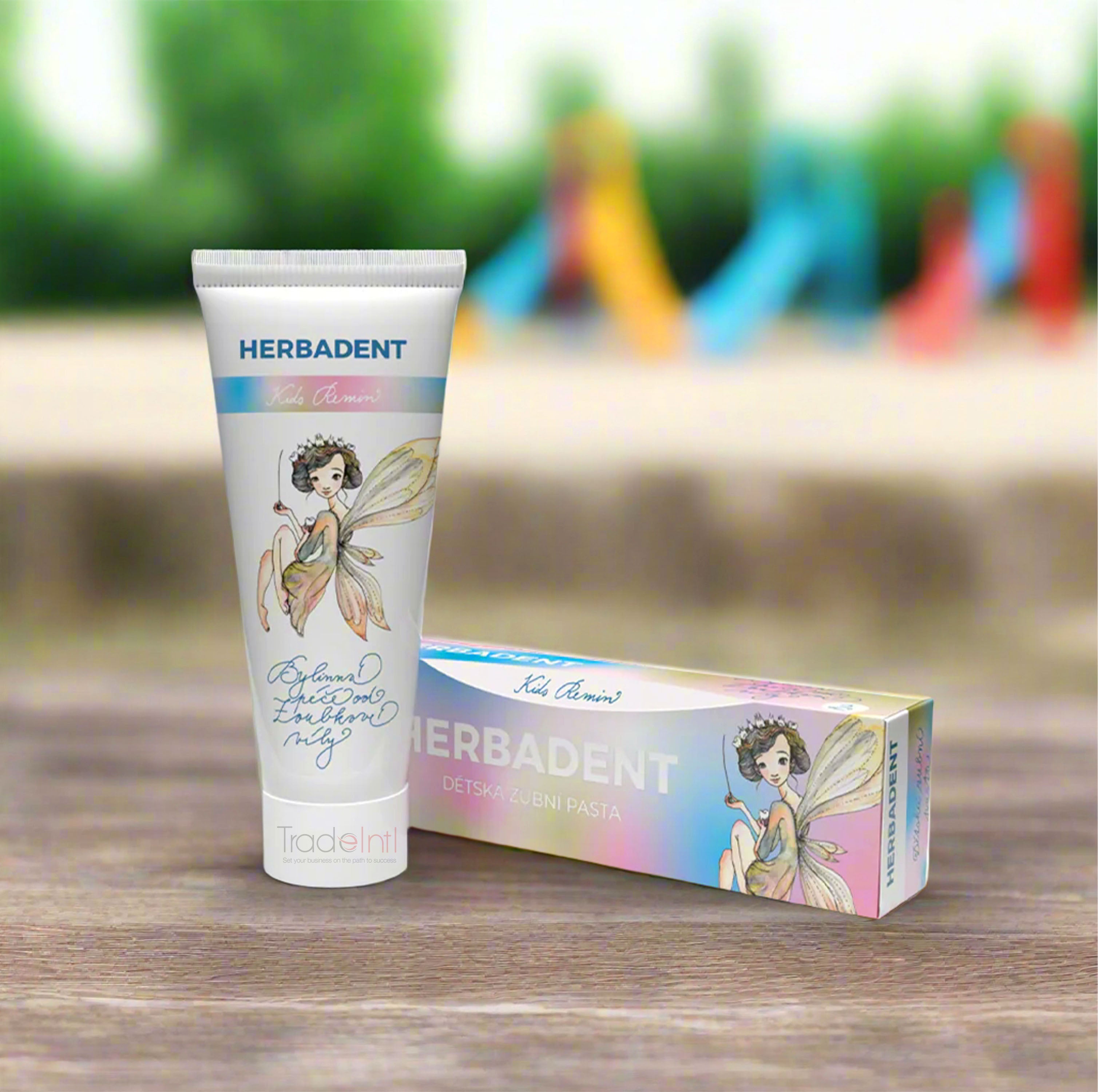 Herbadent children's toothpaste tube and packaging on a wooden surface with a blurred outdoor background.